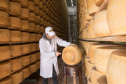 Worker inspecting Parmigiano Reggiano DOP Mitica® 36 months: 7 Ounces in a cheese-aging cell at Athens Cooks, showcasing its artisanal quality and origin.
