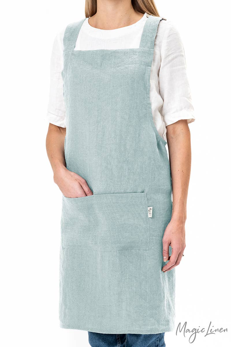 Woman wearing a MagicLinen pinafore cross-back linen apron with front pocket, ideal for cooking and gardening. Perfect blend of style and functionality for kitchen enthusiasts.