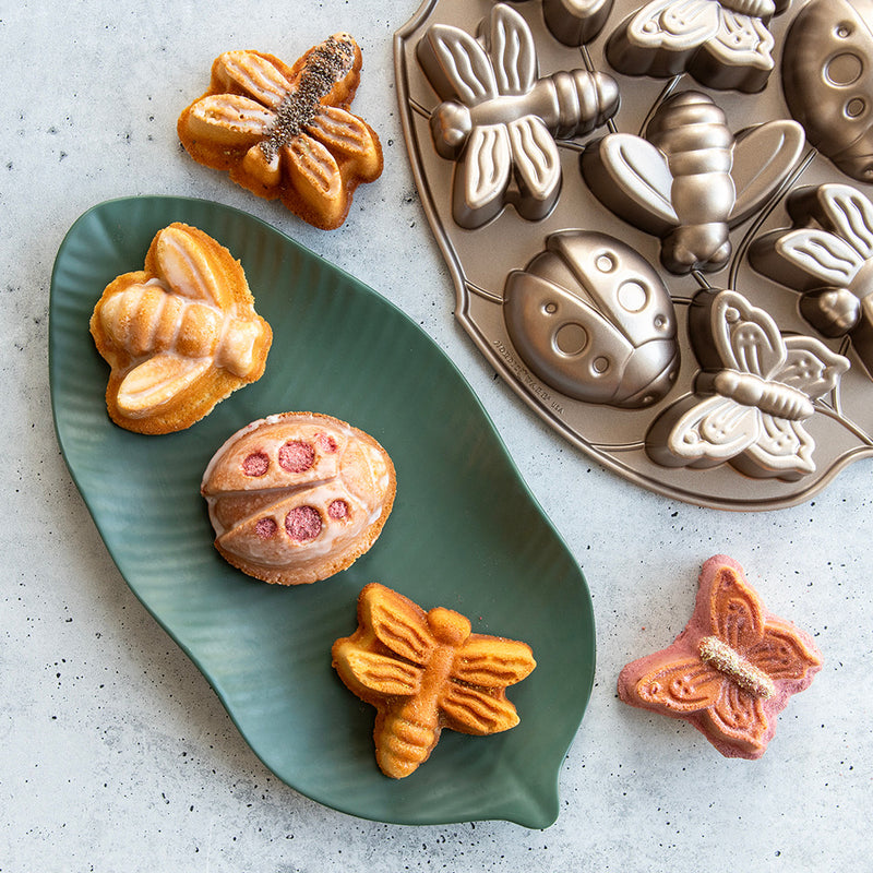 Nordic Ware | Backyard Bugs Pan featuring detailed insect-shaped molds for baking cookies or cakes, perfect for themed parties, displayed with sample pastries on a plate.