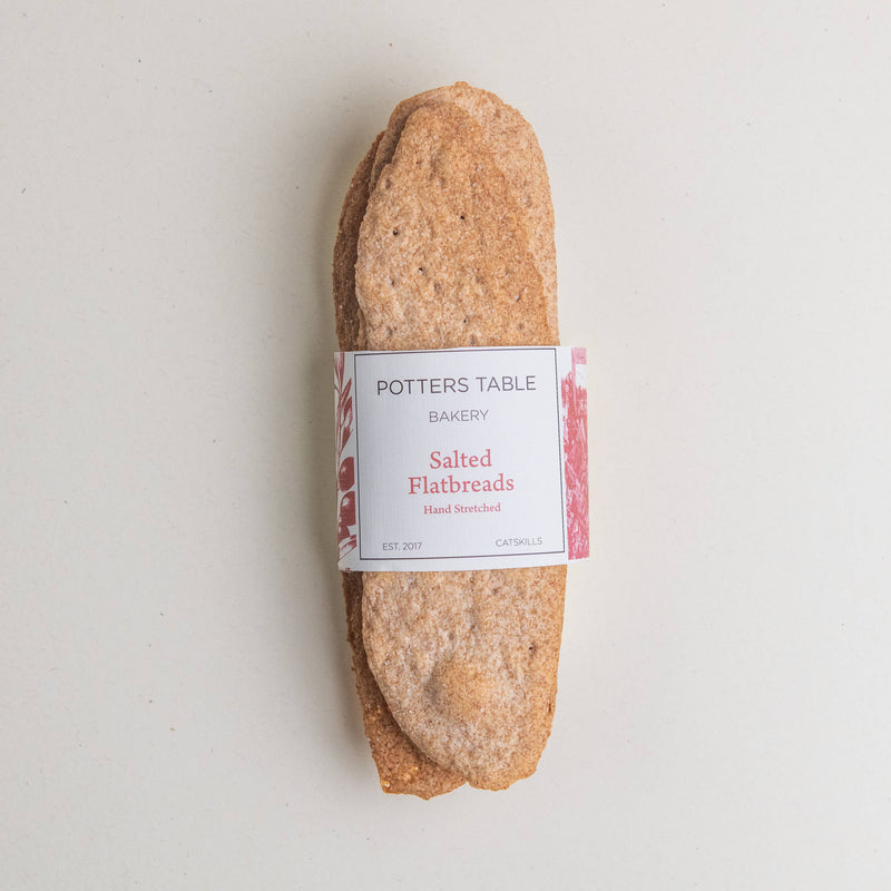 Potters Table - Salted Olive Oil Flatbreads wrapped in a labeled paper band, showcasing hand-stretched, organic whole grain crackers for pairing with cheese or spreads.