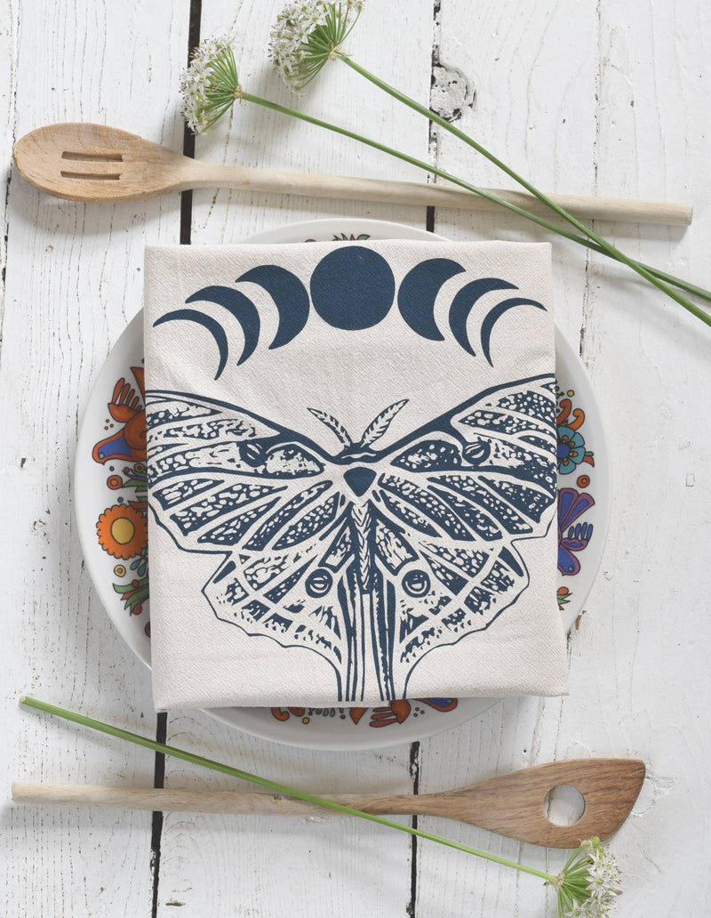Hearth and Harrow - Organic Cotton Luna Moth Tea Towel displayed on a floral plate, accompanied by wooden spoons and wildflowers, showcasing eco-friendly kitchen elegance.