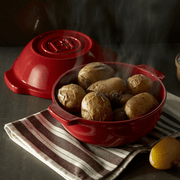Emile Henry | Bread Pot, Charcoal, showcasing steaming, baked potatoes with herbs, on a striped cloth, highlighting its even heat distribution for perfect roasting.