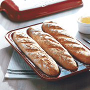 Emile Henry Baguette Baker with loaves on a red tray, showcasing its capability to bake perfect baguettes, ideal for kitchen enthusiasts.