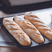 Three golden baguettes cooling on the Emile Henry charcoal ceramic tray