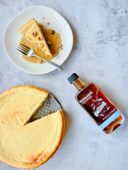 Runamok - Salted Caramel Infused Maple Syrup 250ml next to a plated cheesecake slice drizzled with syrup and garnished with hazelnuts, showcasing its versatile culinary use.