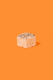 Malvi Mallow - Fluffy Nutter 4-Pack Marshmallows: a single, crumb-topped square showcasing the nutty, chocolate-drizzled treat against an orange backdrop, highlighting its fluffy, artisanal appeal.