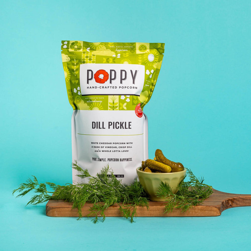 Poppy Hand-Crafted Popcorn - Dill Pickle Popcorn bag on a cutting board, highlighting its tangy, white cheddar, and dill flavor.