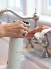 Person using L'AVANT Collective - Fresh Linen Multipurpose Cleaner with a modern trigger spray bottle, ideal for cleaning kitchen and bathroom surfaces.