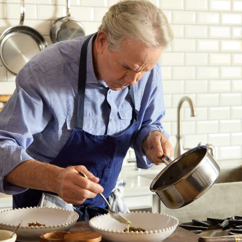 An older man in a kitchen uses a Hestan 1.5qt Saucepan, featuring a resilient, non-toxic titanium surface, to serve food.