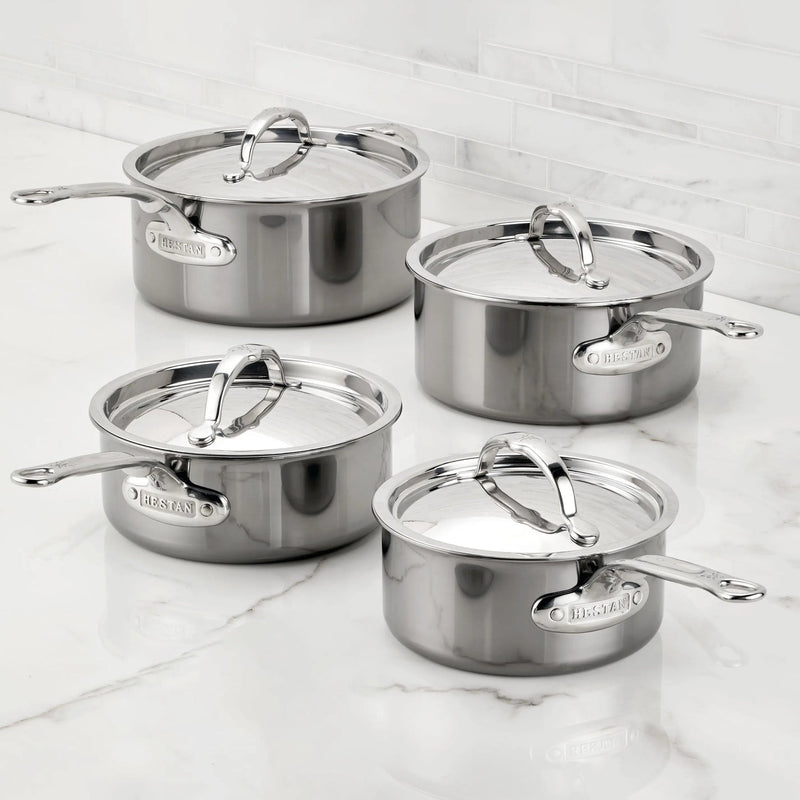 Hestan | Cookware, 1.5qt Saucepan + Lid: Four stainless-steel saucepans with lids, featuring ergonomic handles and Hestan nameplate, displayed on a marble countertop.