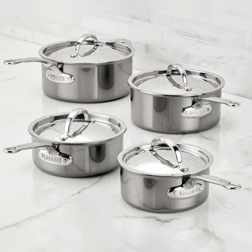 Hestan | Cookware, 1.5qt Saucepan + Lid: Four stainless-steel saucepans with lids, featuring ergonomic handles and Hestan nameplate, displayed on a marble countertop.