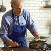 An older man cooking in a kitchen uses the Hestan | Cookware, 3.5qt Sauté Pan + Lid, showcasing its innovative, durable design and ergonomic handle.