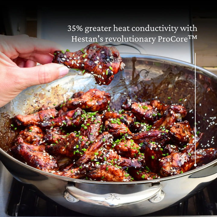 A hand holds chicken in a Hestan Nanobond 14 Wok, showcasing its cooking capabilities, ideal for culinary enthusiasts.