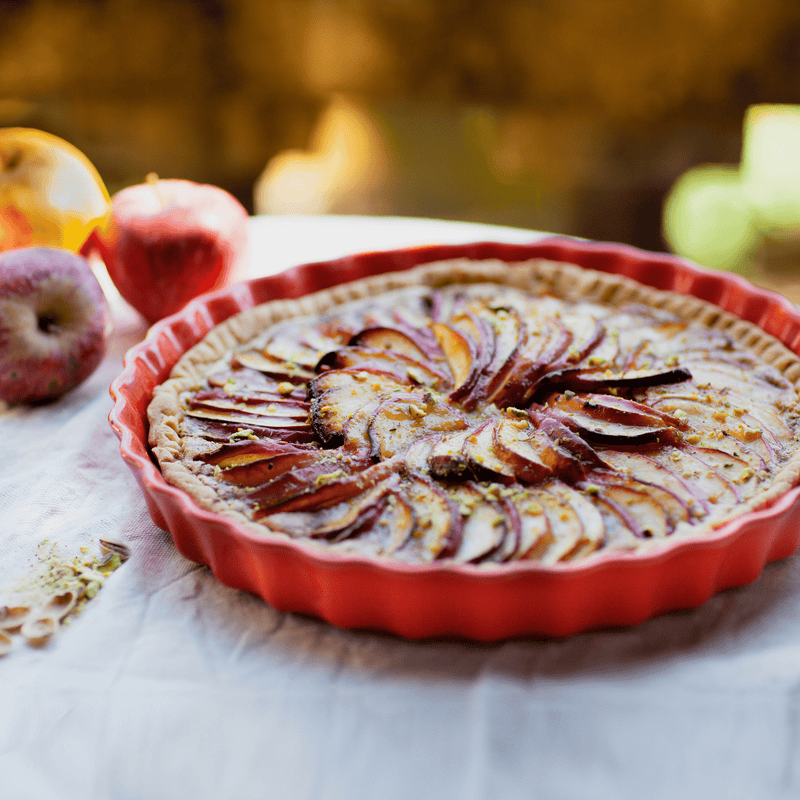 Emile Henry Deep Flan & Tart Dish in use, showcasing a beautifully arranged apple tart with nuts, highlighting its even heat distribution for perfect baking results.