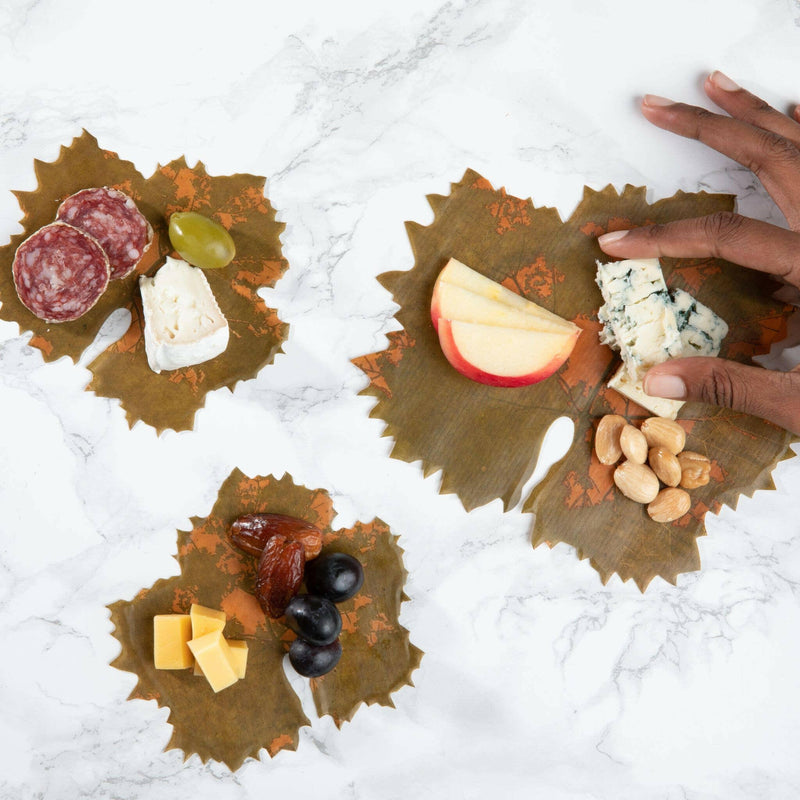 Formaticum | Cheese Board Liners - Large, showcased with cheese and salami slices, ideal for enhancing charcuterie displays, featuring a grape leaf design on wax-coated parchment.