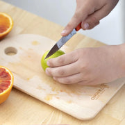 Person slicing lime with Opinel | Essential Serrated Knife, Skyblue, on a wooden board, showcasing its precision and durability for citrus fruits and more.