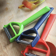 Opinel | T-Duo Peeler, Blue, with dual stainless blades for peeling and julienning, shown on a cutting board with peel remnants, ideal for versatile kitchen tasks.