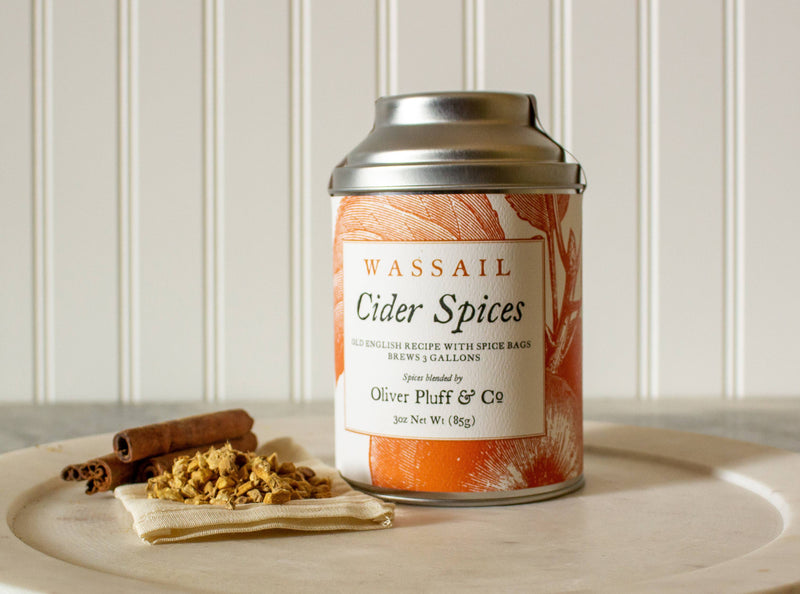 Oliver Pluff & Company - Cider Spices Wassail Kit tin, muslin sachet, and cinnamon sticks on platter, perfect for brewing traditional mulled cider.
