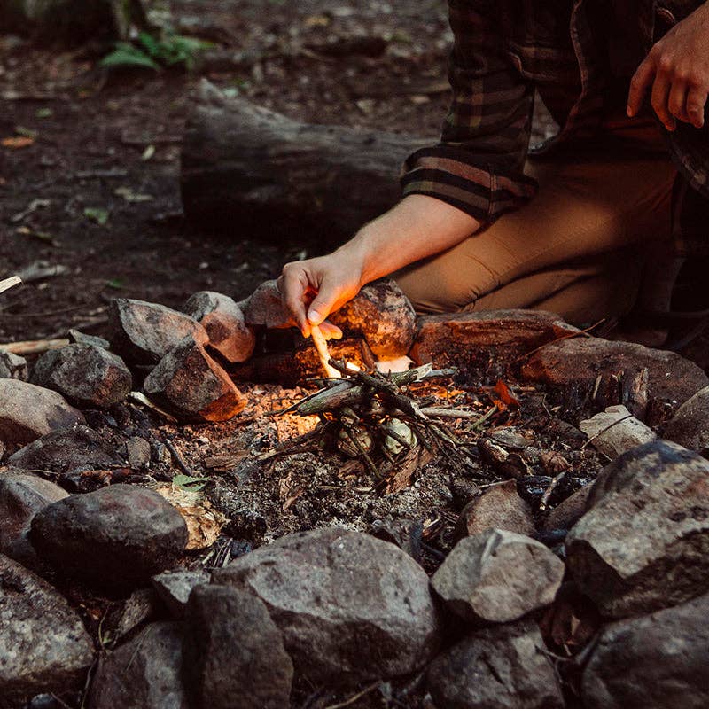 Person igniting a campfire with Bee's Wrap - ReKindle Fire Starters™, emphasizing sustainability and efficient fire starting for outdoor cooking adventures.
