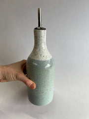 Hand holding the RachaelPots - Oil Cruet Large: Nude/White, a handmade ceramic bottle with a pour spout, ideal for olive oil use.