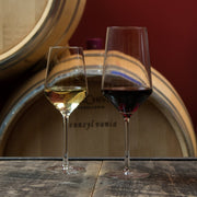 Zwiesel Fortessa | Pure Bordeaux Glass, 23oz: Two elegant stemmed glasses, one with white wine, the other red, on a wooden surface, suggesting a wine-cellar ambiance.