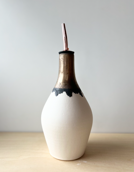 Jessica Wertz Ceramics Gold + White Oil Bottle: A 10 tall unglazed off-white vessel with a bronze-glazed neck, featuring a black stopper and rose-gold straw.