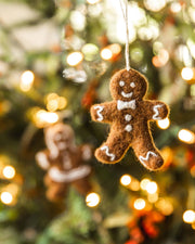 Farmhouse Pottery - Felted Gingerbread Ornament: Lady, a handcrafted brown gingerbread figure with white icing details, hangs against a festive, softly lit Christmas tree backdrop.