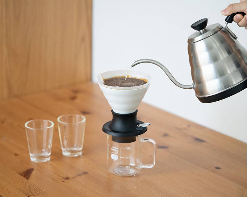 HARIO USA - HARIO Ceramic Immersion Dripper 02 SWITCH in use with a gooseneck kettle, showcasing a precise pour-over coffee setup on a wooden table.