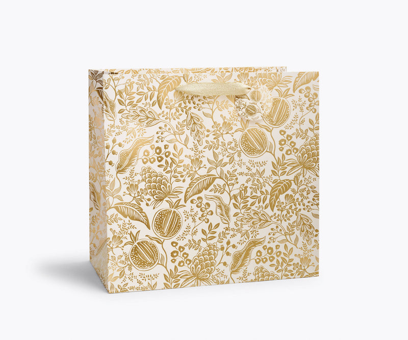 Rifle Paper Co. - Pomegranate Gift Bag: Wine, featuring a cream background with metallic gold botanical patterns and gold ribbon handles, perfect for elegant gift-giving.