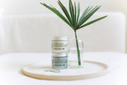 Little Seed Farm deodorant creams, Grapefruit Lemon and Activated Charcoal, on a tray with a palm leaf in a bottle; nourishing, organic skincare essentials.