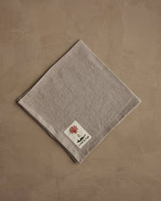 Coral & Tusk - Sunflower and Wheat Dinner Napkin, featuring a red coral label, folded on a beige surface, perfect for autumn harvest table settings.