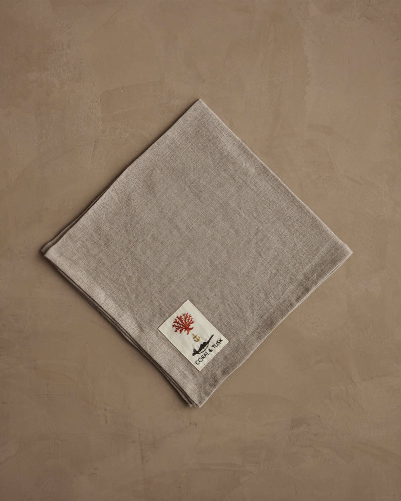 Coral & Tusk - Autumn Blossoms Dinner Napkin with floral embroidery, folded on a taupe surface, featuring a red coral label. Ideal for elegant fall dining settings.