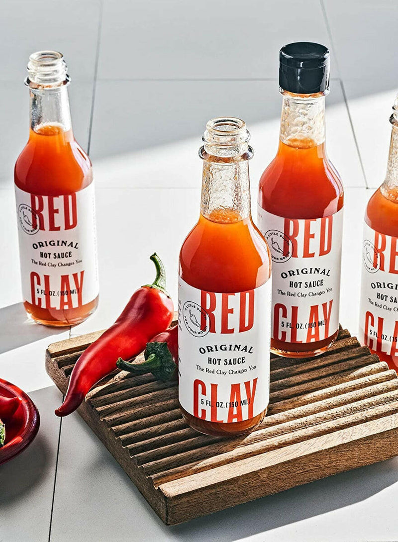 Red Clay | Carolina Hot Sauce bottle on a wooden board, highlighting its Southern-inspired flavor profile with pequin and cayenne peppers, perfect for enhancing any dish.