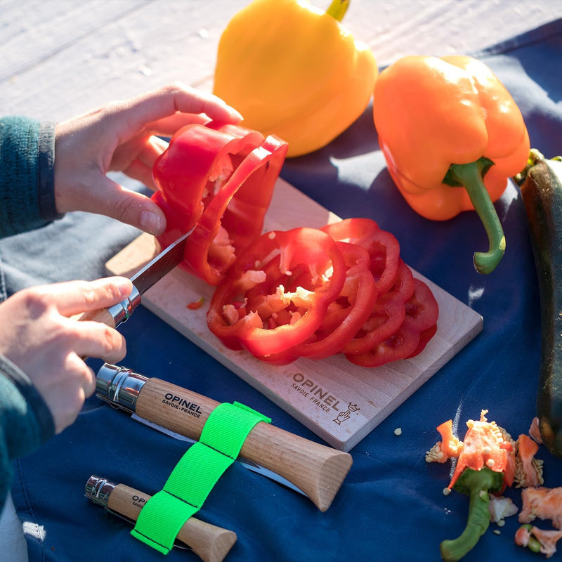 The Opinel | Nomad Cooking Kit showcases a wooden-handled knife slicing a red pepper, with additional knives and vegetables on a branded cutting board.