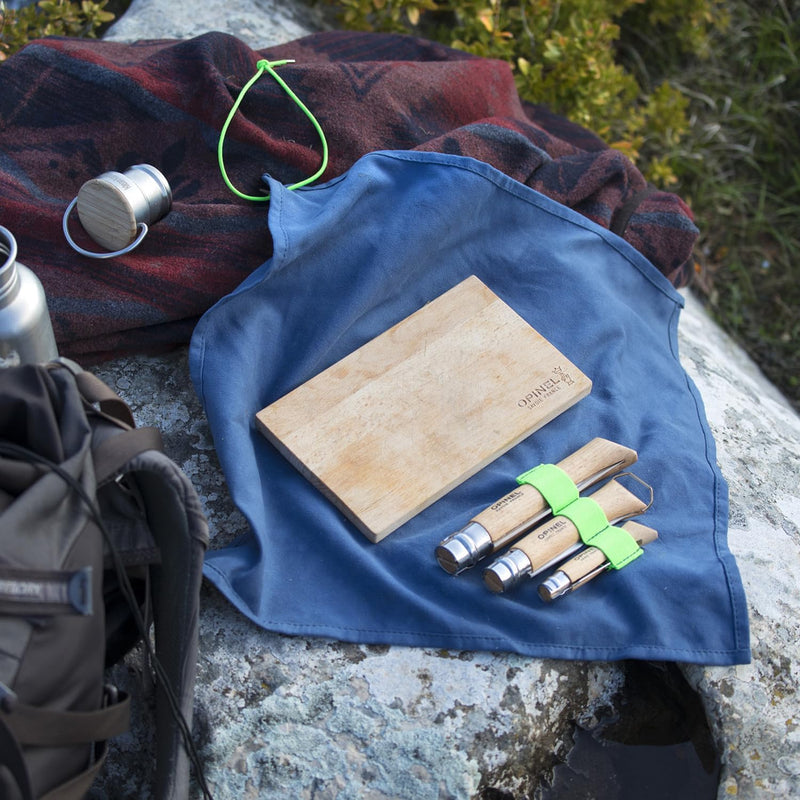 Opinel | Nomad Cooking Kit staged on a rock, featuring folding knives, a cutting board, and accessories, perfect for outdoor meal prep.