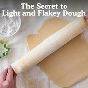 Person rolling dough with a rolling pin on a Natural Pastry Cloth & Rolling Pin Cover in a kitchen, highlighting its use for baking preparation.