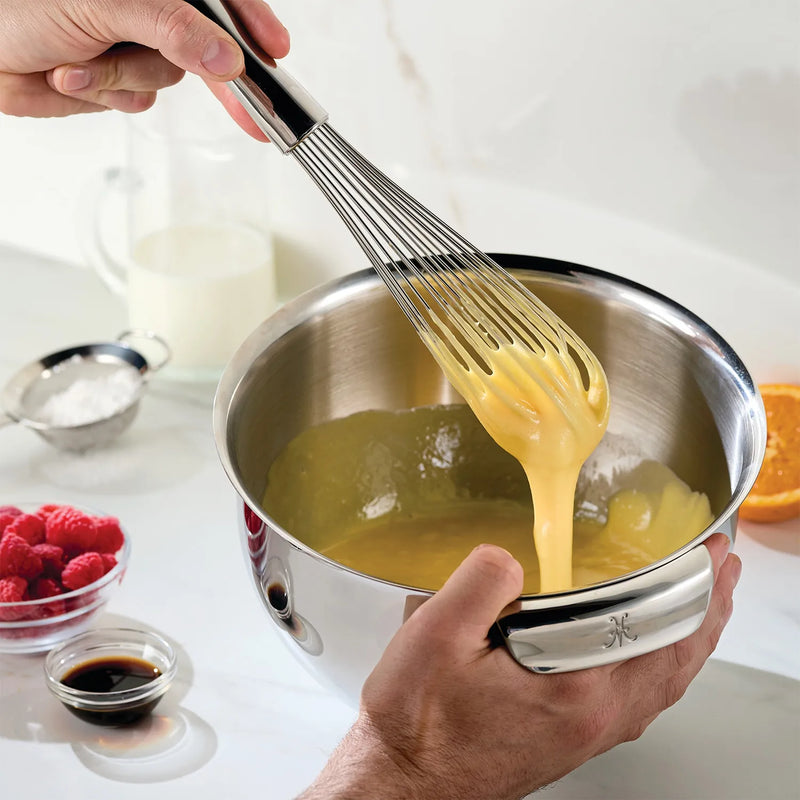Person mixing in Hestan 4pc Stainless Steel Mixing Bowl Set, featuring sizes from 1.5qt to 7.0qt, with whisk and food visible.