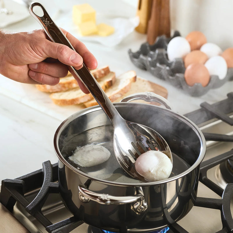 Person using Hestan 13 Stainless Steel Slotted Spoon over a pot, showcasing its effectiveness for cooking tasks in a kitchen setting.