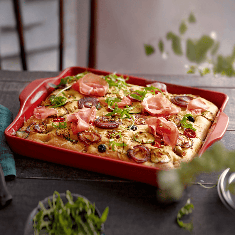 Emile Henry Focaccia + Detroit Pizza Pan, 6 x 12.5, Burgundy, showcasing fresh focaccia with zucchini, red onion, cherry tomatoes, olives, pine nuts, arugula, and prosciutto.