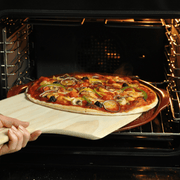 Hand uses Emile Henry Ridged Pizza Stone to slide topped pizza into oven, highlighting its easy handling and performance for perfect home-crisped crusts.