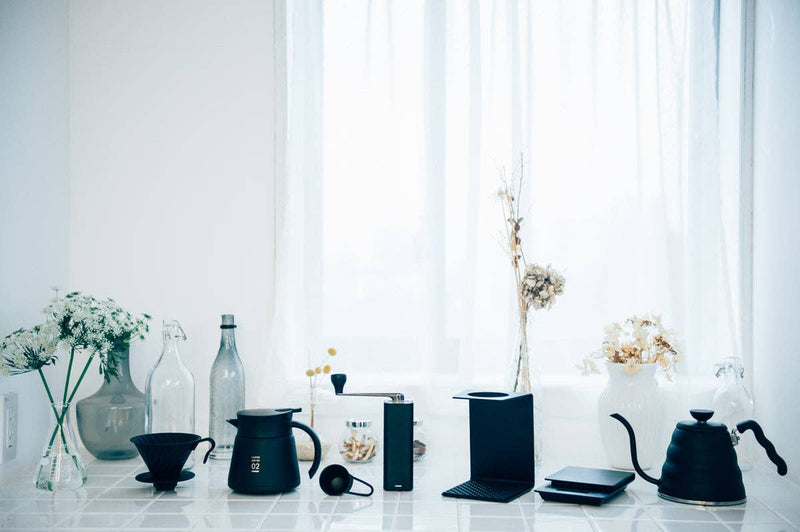 V60 Metal Dripper by HARIO USA on a minimalist kitchen counter, surrounded by coffee tools, highlighting its precision design for enhanced brewing.