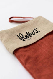 MagicLinen - Embroidered Christmas Stocking with Roberti in black script, crafted from rust and beige linen, featuring a hanging loop for festive display.