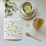 Ink and Fiber Designs - Wildflowers Swedish Dishcloth displayed with a cup of tea, lemon, and honey, ideal for eco-friendly kitchen cleaning.