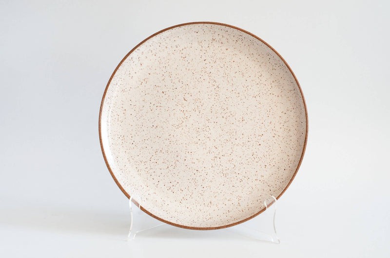 RachaelPots - Serving Platter: Sage, a round, speckled ceramic plate with a brown rim, displayed upright, showcasing its handcrafted elegance for enhancing dinner presentations.