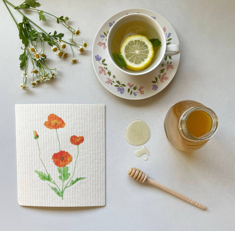 Ink and Fiber Designs - California Orange Poppy Swedish Dishcloth near a cup of tea, lemon, and honey, highlighting its absorbency and eco-friendly features.