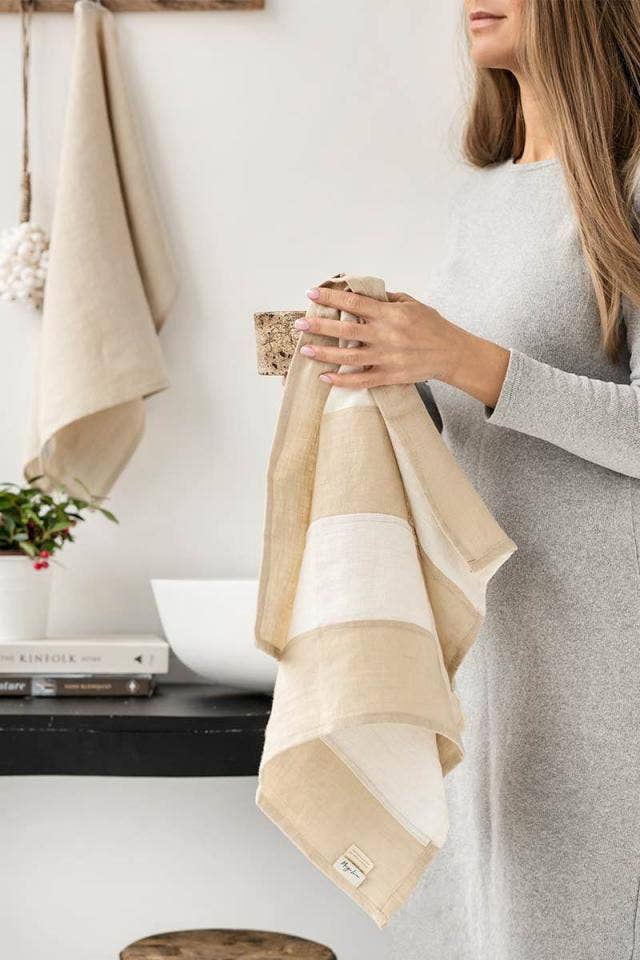 Woman holding MagicLinen's striped linen tea towel, showcasing its soft, durable fabric and convenient hanging loop, ideal for kitchen use. Part of a zero-waste program.