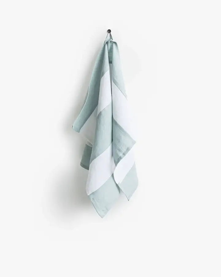 Striped linen tea towel hangs on a hook, showcasing its loop for easy storage. Part of a zero-waste initiative, ideal for stylish and practical kitchen use.