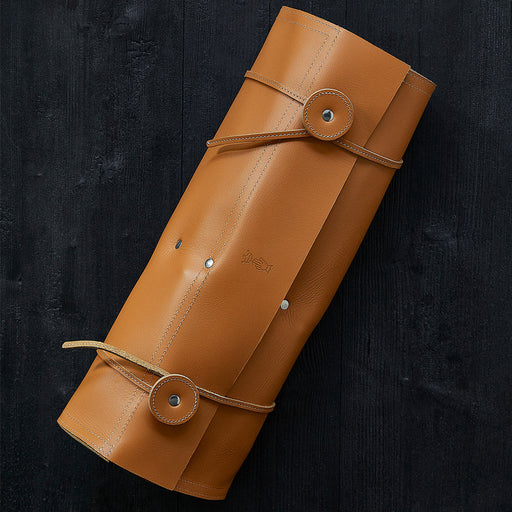 Opinel | 8 Slot Chef Knife Carrier, Leather: A tan leather roll-up pouch designed for storing chef knives, featuring stitched straps and snap buttons on a dark wooden surface.