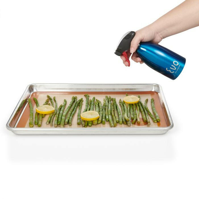 Hand holding Evo Stainless Steel Oil Sprayers - Purple, spraying oil over asparagus on a tray, showcasing precise, non-aerosol distribution for healthier cooking.