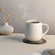 OHOM - Ui 3 Self-heating Mug Set: Jasmine White on a warming coaster, with a vase of dried flowers and an open book nearby.
